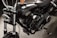 A close-up view of a black motorcycle, focusing on the engine and components. The chrome and metallic parts are polished, with the brand name prominently displayed on the side. The background appears to be a dark, textured surface.