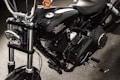 A close-up view of a black motorcycle, focusing on the engine and components. The chrome and metallic parts are polished, with the brand name prominently displayed on the side. The background appears to be a dark, textured surface.