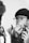A person with glasses and a beanie is using an electric trimmer to shave facial hair while looking in a mirror. Their expression appears focused as they groom their chin, with one hand holding the trimmer and the other touching their face.