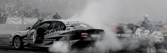 A dynamic shot of the black and red RC foam track with a banked straightaway, filled with 1/28 scale RC cars racing indoors under bright lights.