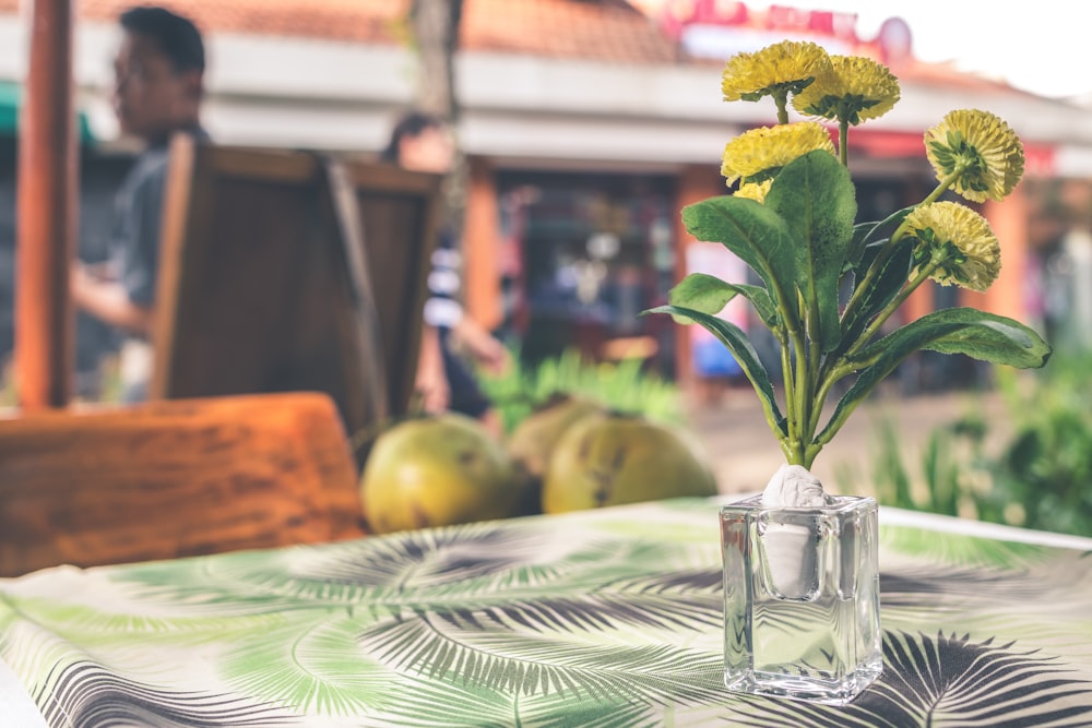 eine mit gelben Blumen gefüllte Glasvase auf einem Tisch