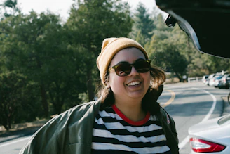 A stylish person wearing bright yellow glasses, smiling outdoors on a sunny day.