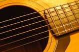 A close-up view of an acoustic guitar highlighting the strings, fretboard, and sound hole. The warm wood tones on the guitar body create a vintage appearance.