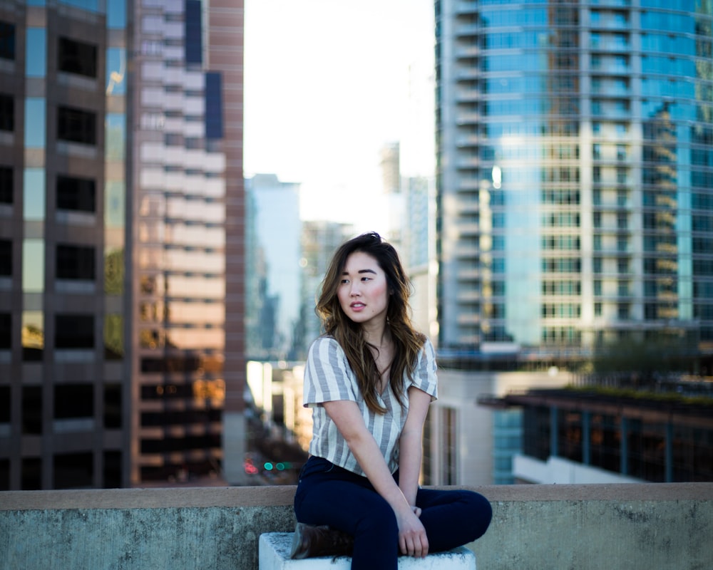 건물 가장자리 근처에 앉아있는 회색 셔츠를 입은 여자의 선택적 초점 사진
