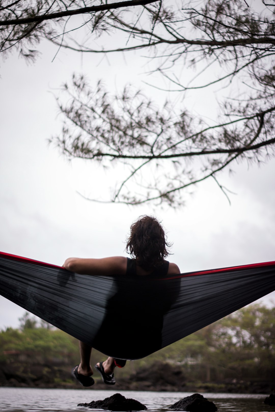 woman sitting on hammock facing body of water