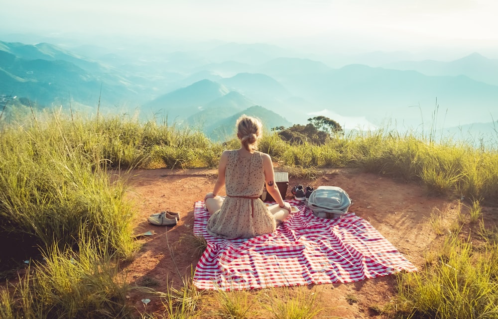 Mujer con vestido gris sin mangas sentada en la alfombra de picnic