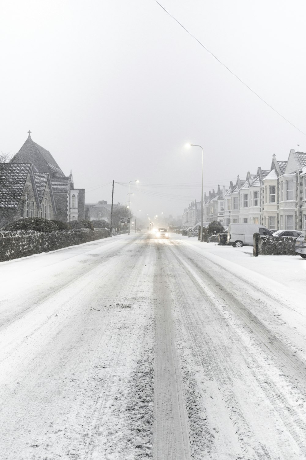 Schneebedeckte Straße zwischen Dorf und Fahrzeugen