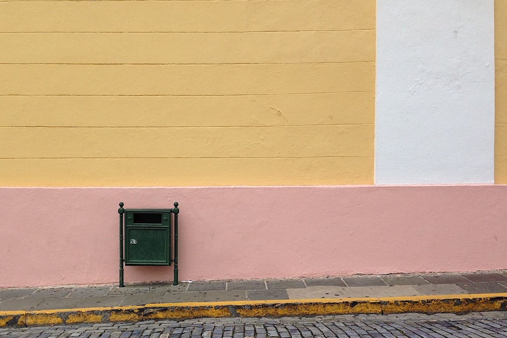 Caixa de correio verde ao lado da parede rosa