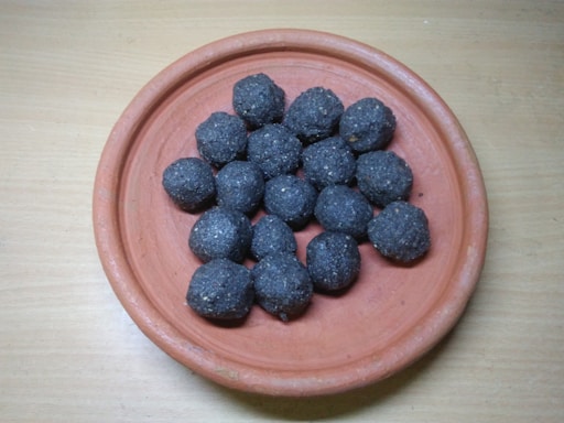 A terracotta plate holds several round, black food items that are evenly distributed. The surface underneath the plate is a light brown, wooden texture.