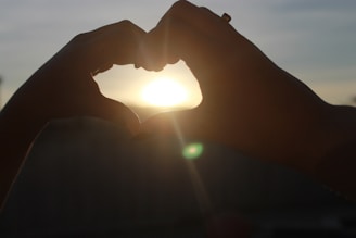 Hands releasing a glowing heart-shaped light into a twilight sky filled with stars.