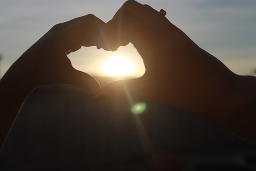 Hands releasing a glowing heart-shaped light into a twilight sky filled with stars.
