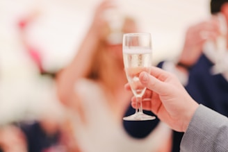 A close-up of a hand holding a glass of vintage champagne with a soft charcoal background.