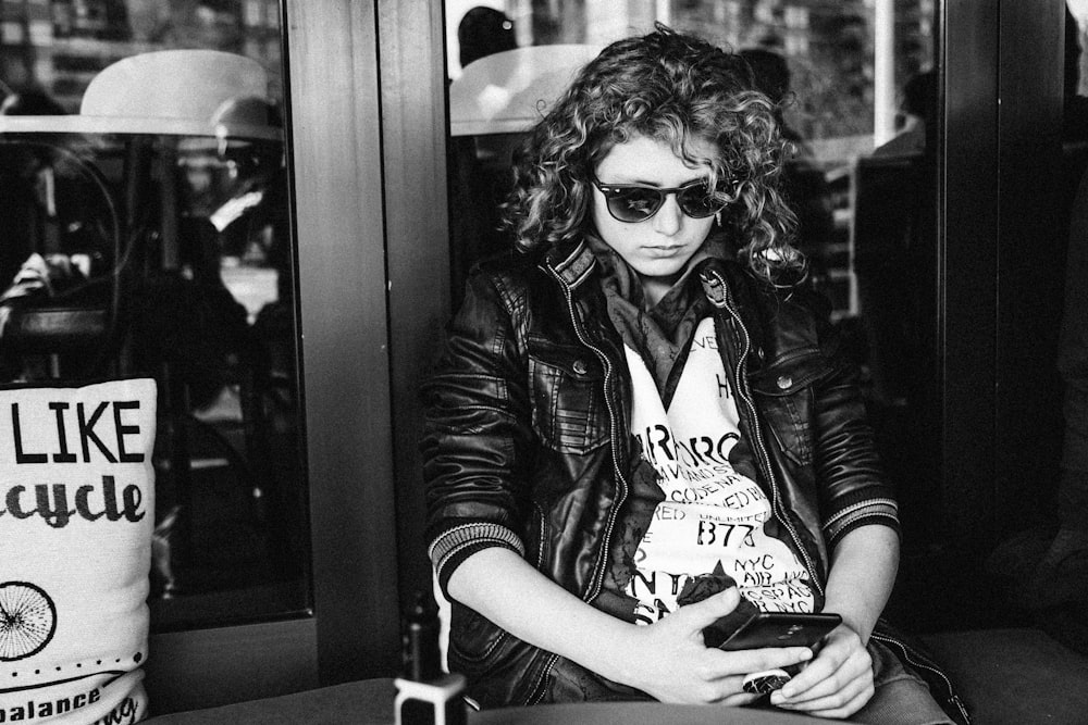 greyscale photo of sitting woman using smartphone