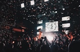 A lively concert scene with a band performing on stage, surrounded by an enthusiastic crowd. Confetti fills the air as bright stage lights illuminate the musicians and the audience. The atmosphere is vibrant, with people capturing the moment on their phones.