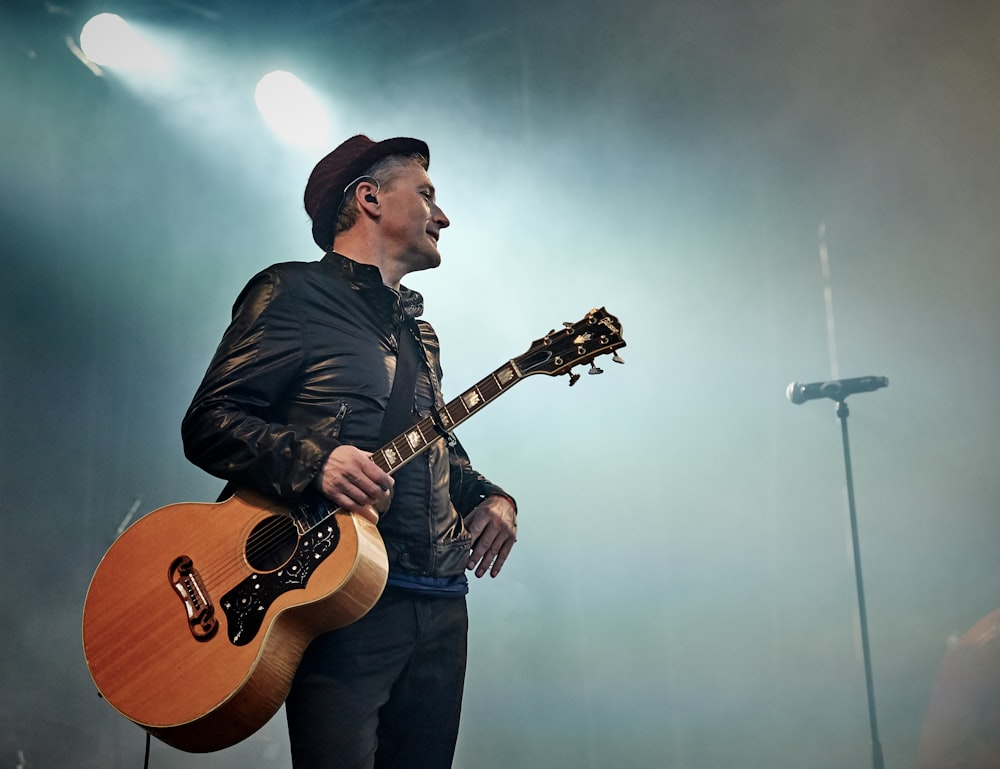 man holding acoustic guitar beside microphone with stand