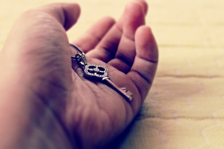 A close-up image of a hand holding an ornate key. The hand is open, resting on a soft, light-colored surface, giving a sense of calmness and introspection. The intricate details of the key suggest significance or value.