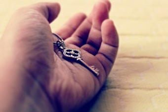 A close-up image of a hand holding an ornate key. The hand is open, resting on a soft, light-colored surface, giving a sense of calmness and introspection. The intricate details of the key suggest significance or value.