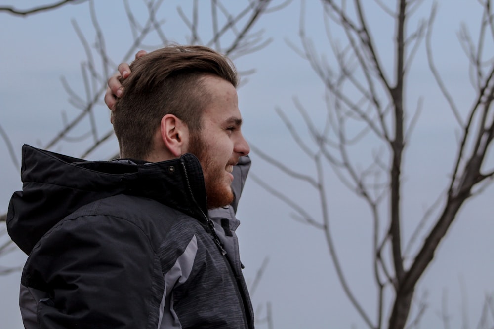 man in black jacket standing near bare trees