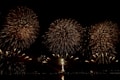 A vibrant display of large fireworks bursts fill the dark night sky with bright, sparkling patterns. The image captures multiple golden explosions of light radiating outwards, creating a celebratory and festive atmosphere.