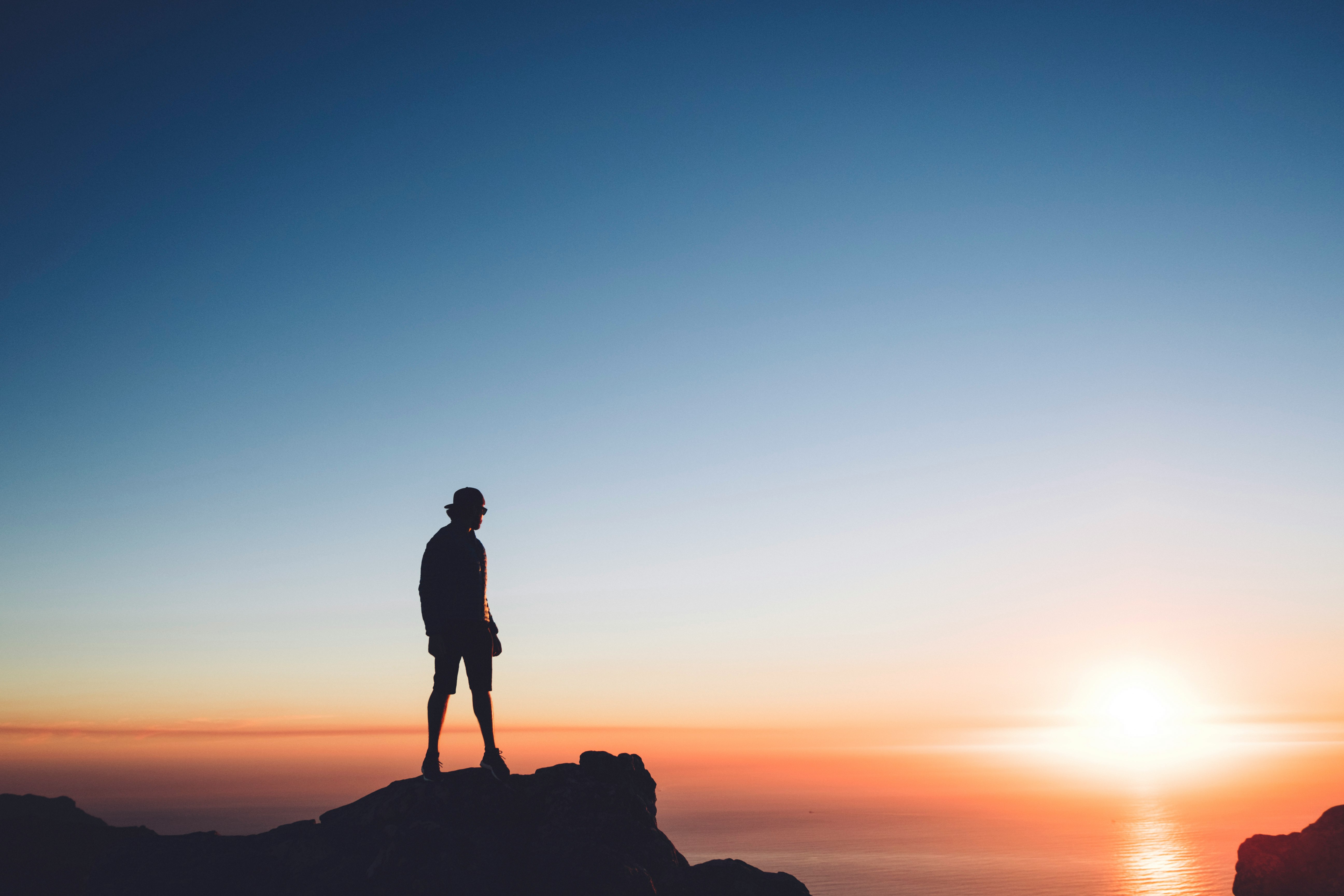 silhouette photo of man standing on peak front of the sea