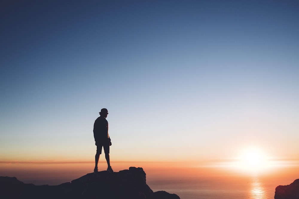 silhouette photo of man standing on peak front of the sea