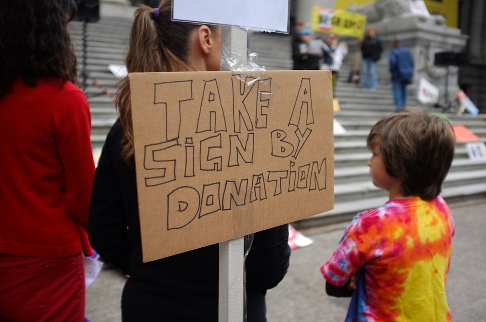 boy standing beside take a sign by donation board