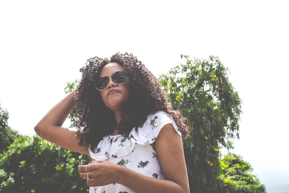 woman with sunglasses standing near green leafed tree outdoor during daytime