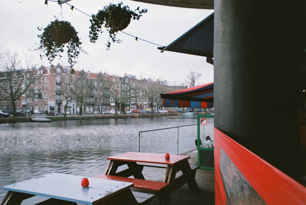 Outdoor riverside dining area with cozy wooden tables and soft string lights at sunset.