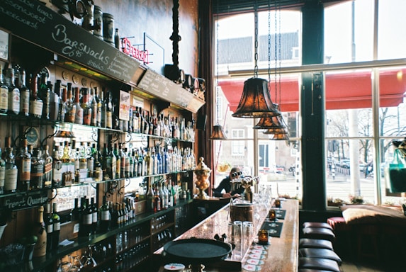 Cozy bar counter with warm lighting and bottles neatly arranged on shelves.