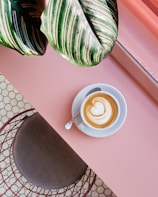 cup of coffee on saucer with teaspoon on pink tabletop