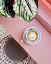 cup of coffee on saucer with teaspoon on pink tabletop