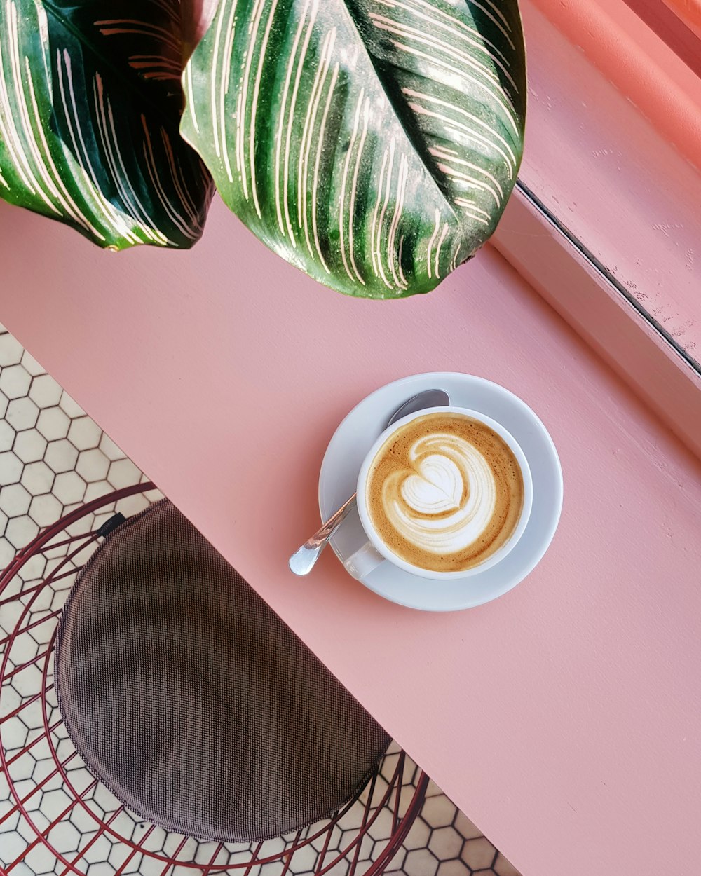 Tasse Kaffee auf Untertasse mit Teelöffel auf rosa Tischplatte