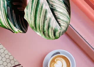 cup of coffee on saucer with teaspoon on pink tabletop