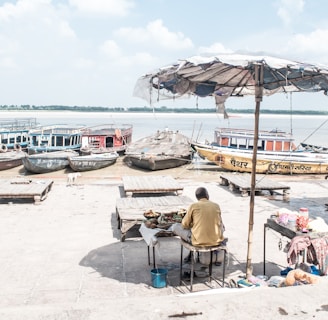 photo of man under patio umbrella near body of water