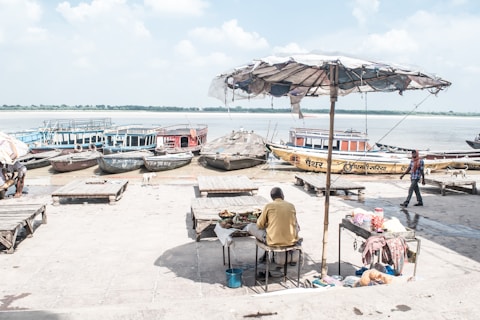 photo of man under patio umbrella near body of water