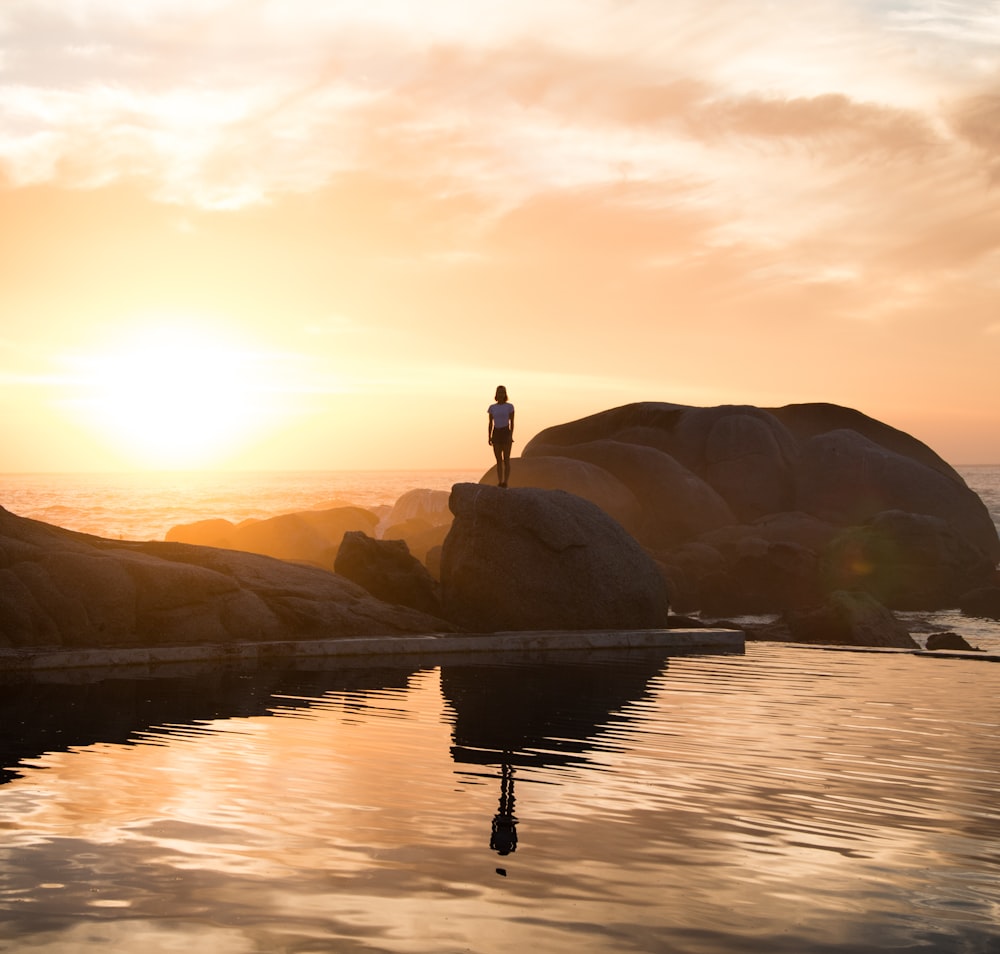 woman standing on a gray rock near body of water