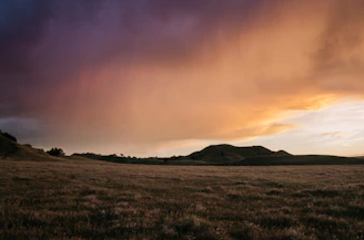 A peaceful landscape featuring clouds rolling over green hills at sunset.