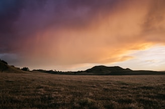 A serene landscape featuring rolling hills under a dramatic sky at sunset.
