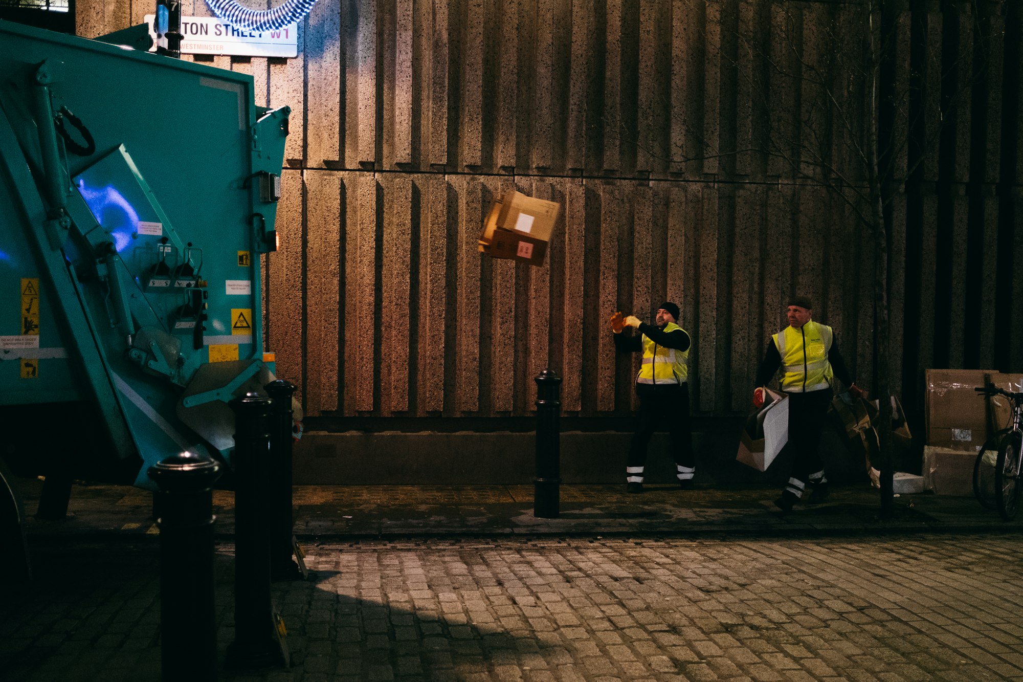two man standing beside the building throwing garbage into a truck