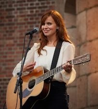 Young woman playing an acoustic guitar on a sunlit stage.