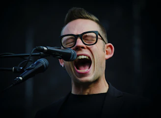 A smiling student singing into a microphone during a voice lesson.