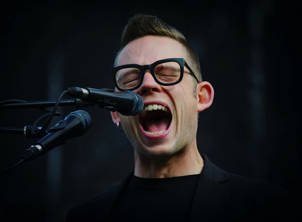 A smiling student singing passionately during an online vocal lesson on a laptop screen.