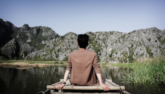 man sitting on brown dock in front of gray rock formation
