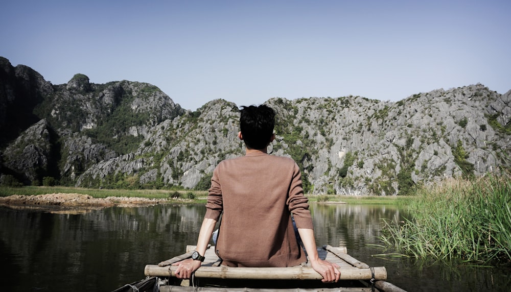 Homme assis sur un quai brun devant une formation rocheuse grise