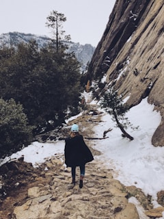 Close-up of a hand-knit beanie with earthy tones, worn by someone hiking a mountain trail.