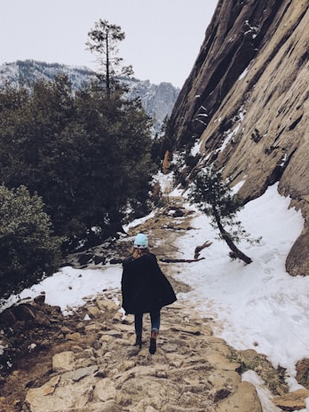 Close-up of a hand-knit beanie with earthy tones, worn by someone hiking a mountain trail.