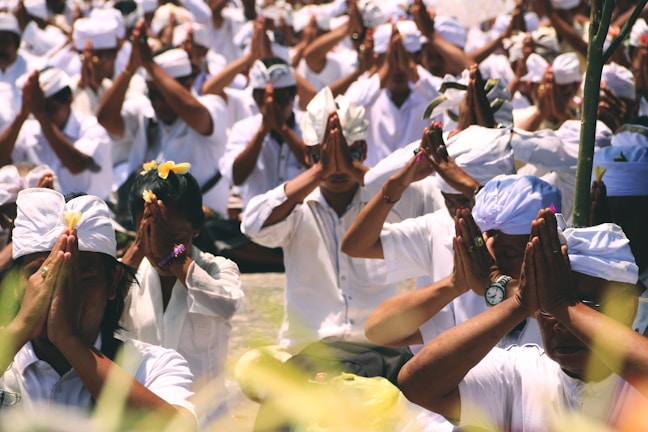 A peaceful outdoor ceremony with white fabrics, flowers, and participants praying.