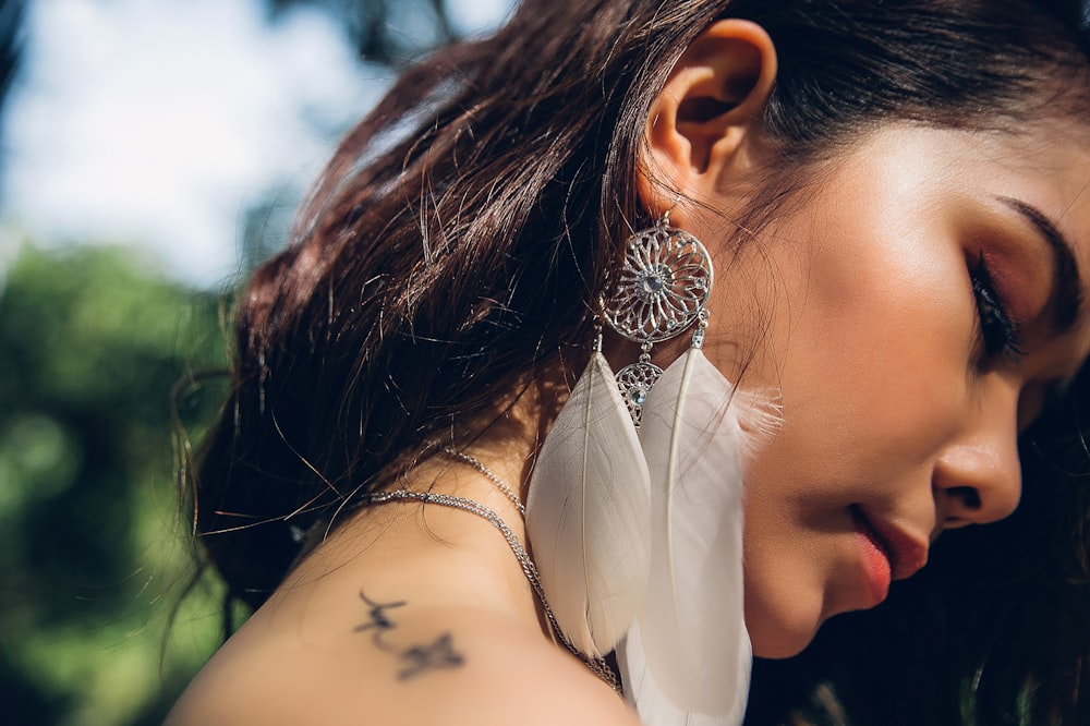 selective focus photo of woman wearing silver-colored and white feather earring