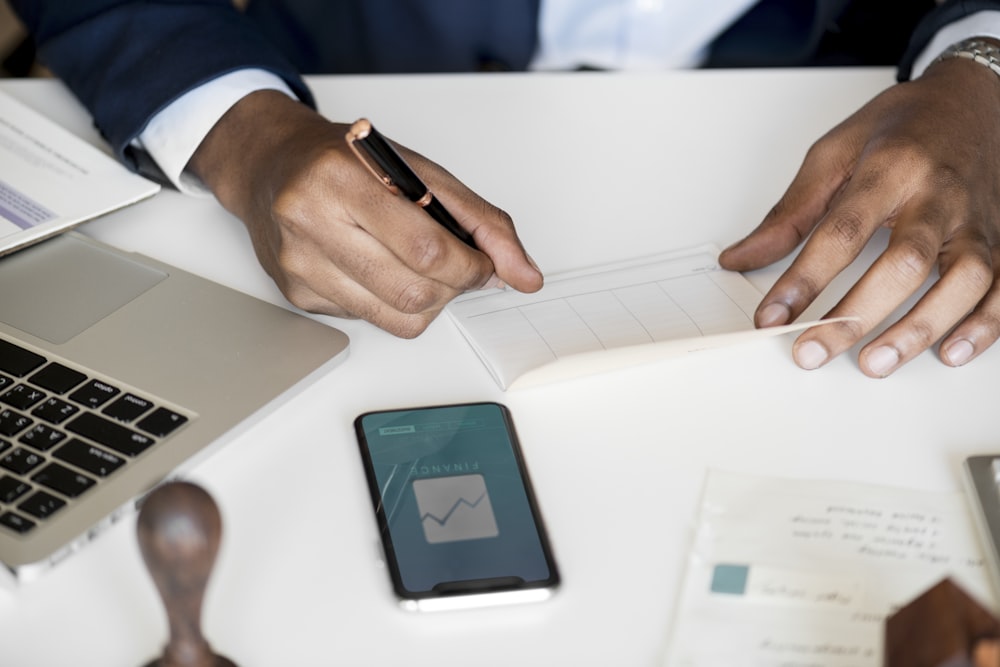 person writing on paper while holding black twist pen on white table