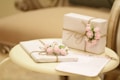 Elegant white gifts adorned with pink rose decorations are tied with rustic twine, resting on a round, cream-colored table next to a piece of stationery.